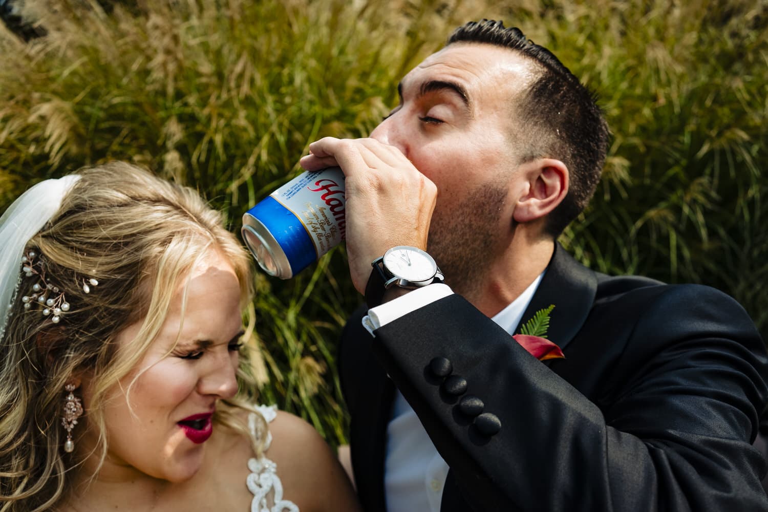 A colorful, candid picture of a man drinking from a Hamm's beer can as a bride grimmaces nearby on a fall wedding day. 