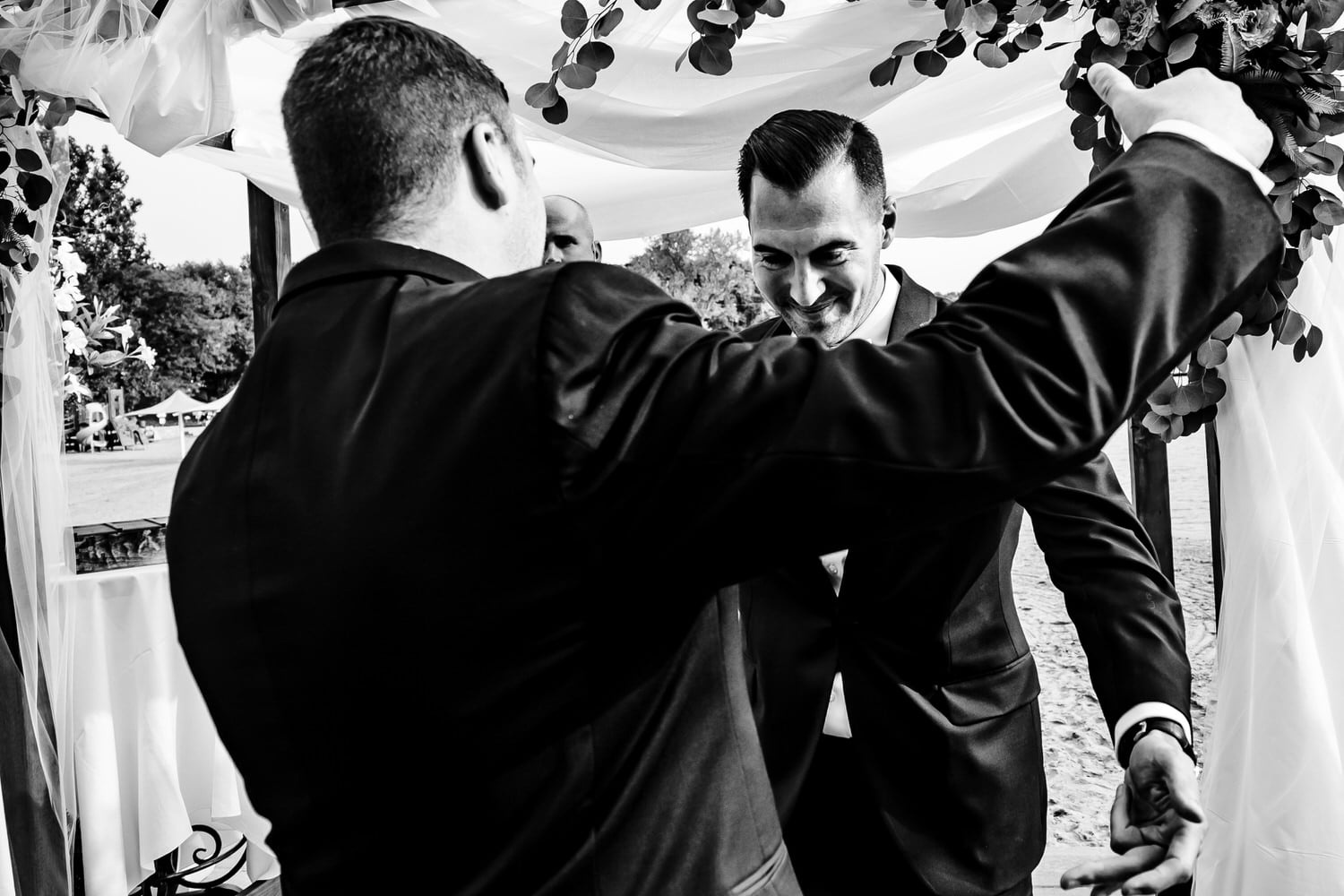 A candid black and white picture of a groom leaning in to hug a groomsmen as he walks down the aisle during a fall wedding ceremony at Lake Quivira Country Club in Kansas City. 
