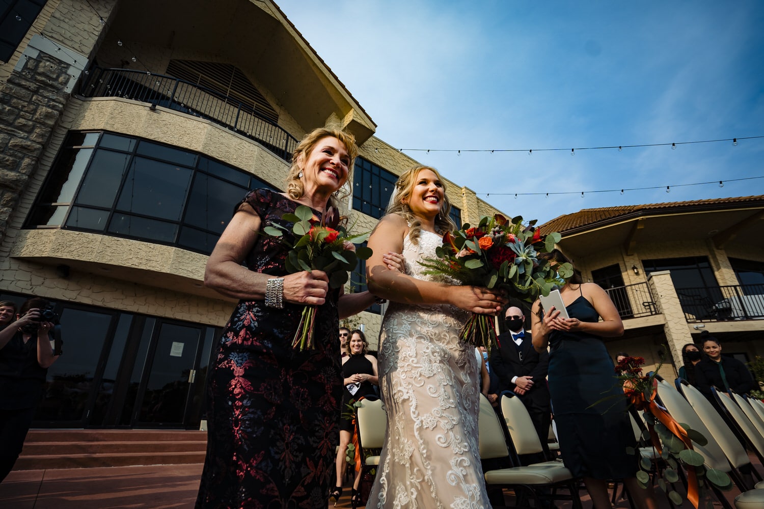 A candid, colorful picture of a bride and her mom walking down the aisle during a fall wedding ceremony at Lake Quivira Country Club in Kansas City. 