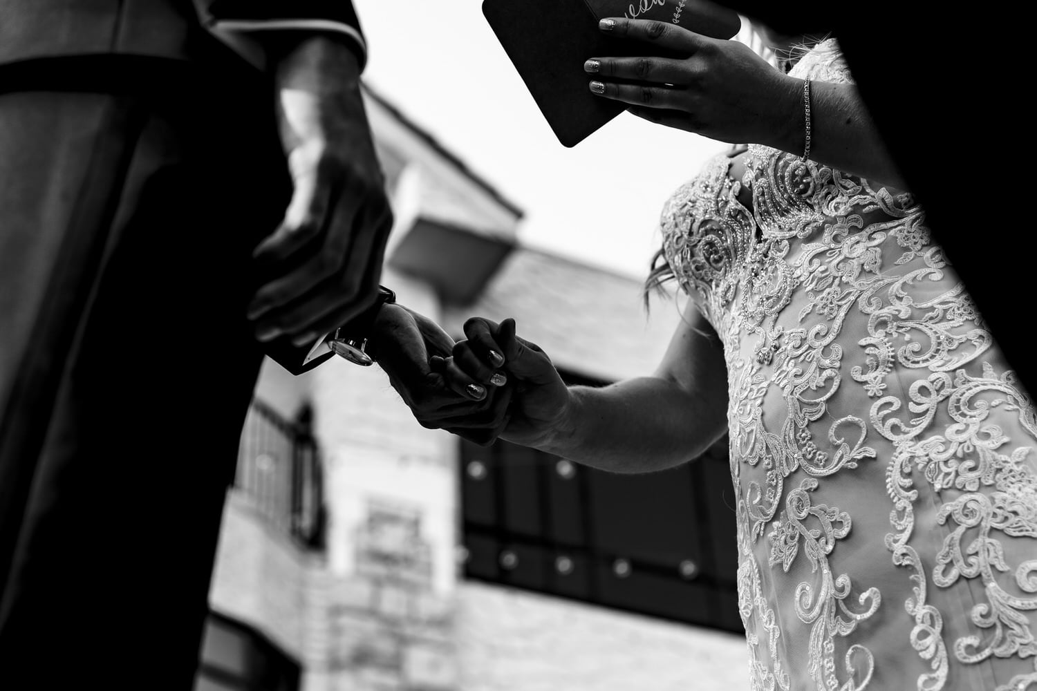 A candid black and white picture looking up as a bride and groom hold hands during their wedding ceremony as the bride reads her wedding vows to her groom. 