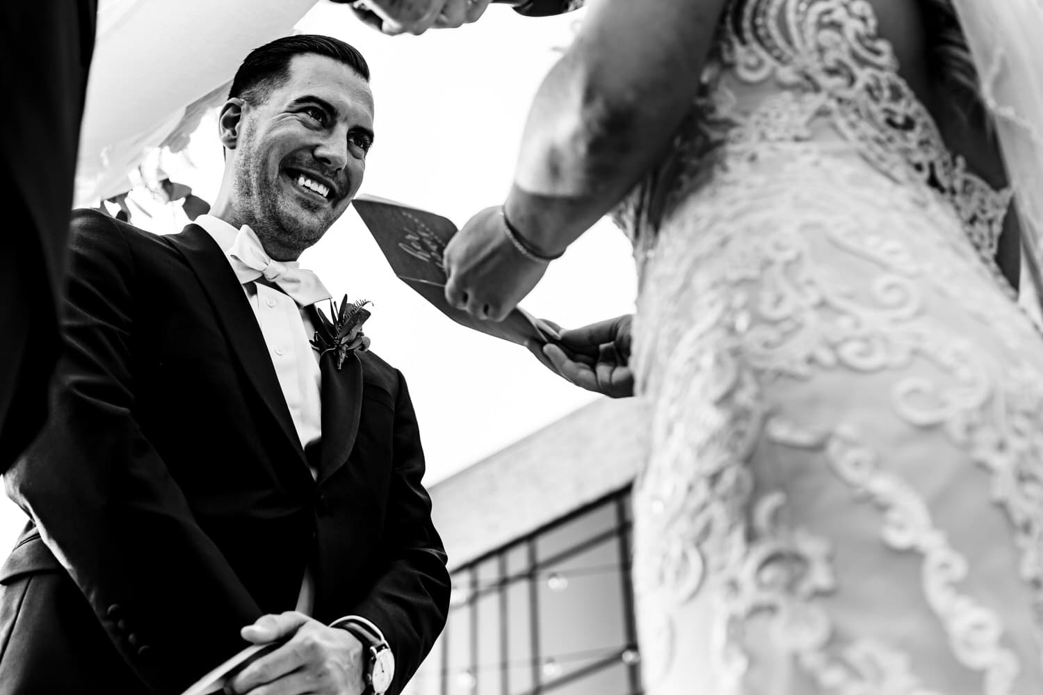 A candid black and white picture looking up as a bride and groom hold hands during their wedding ceremony as the bride reads her wedding vows to her groom. 