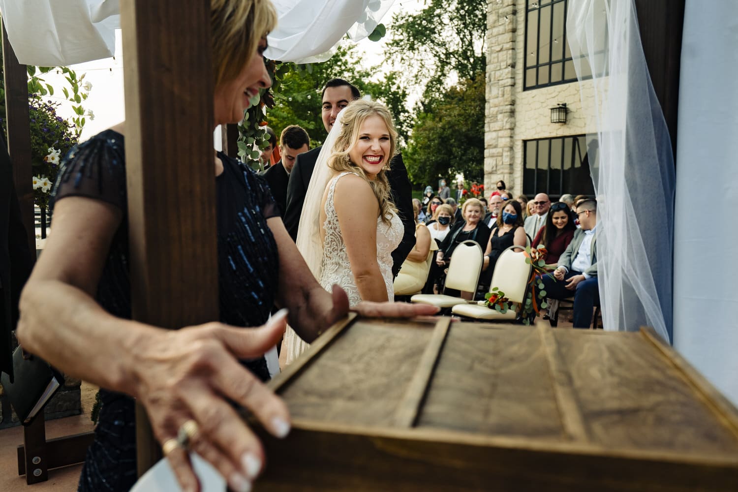 A candid picture of a bride and groom smiling at a groom's mom as she puts the lid on a wooden wine box during a fall wedding ceremony in Kansas City at Lake Quivira Country Club. 