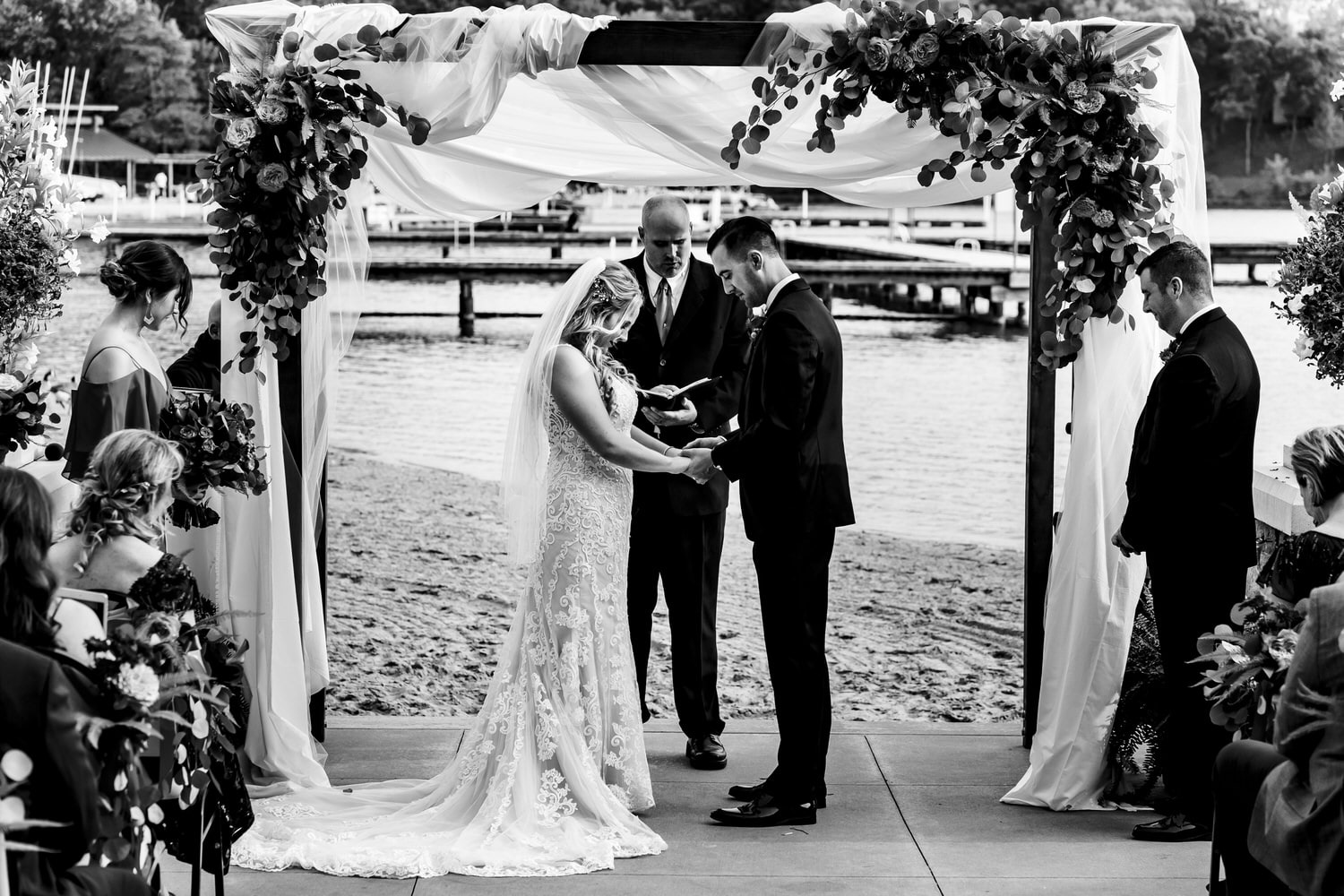 A candid black and white picture of a bride and groom holding hands in prayer during a wedding ceremony at Lake Quivira Country Club in Kansas City. 