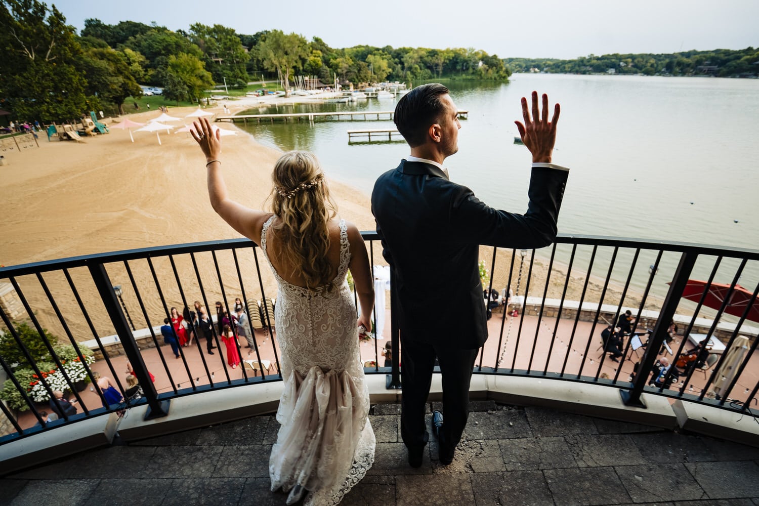 A candid picture of a bride and groom standing on a balcony, waving to their wedding guests below on a fall wedding day at Lake Quivira Country Club. 