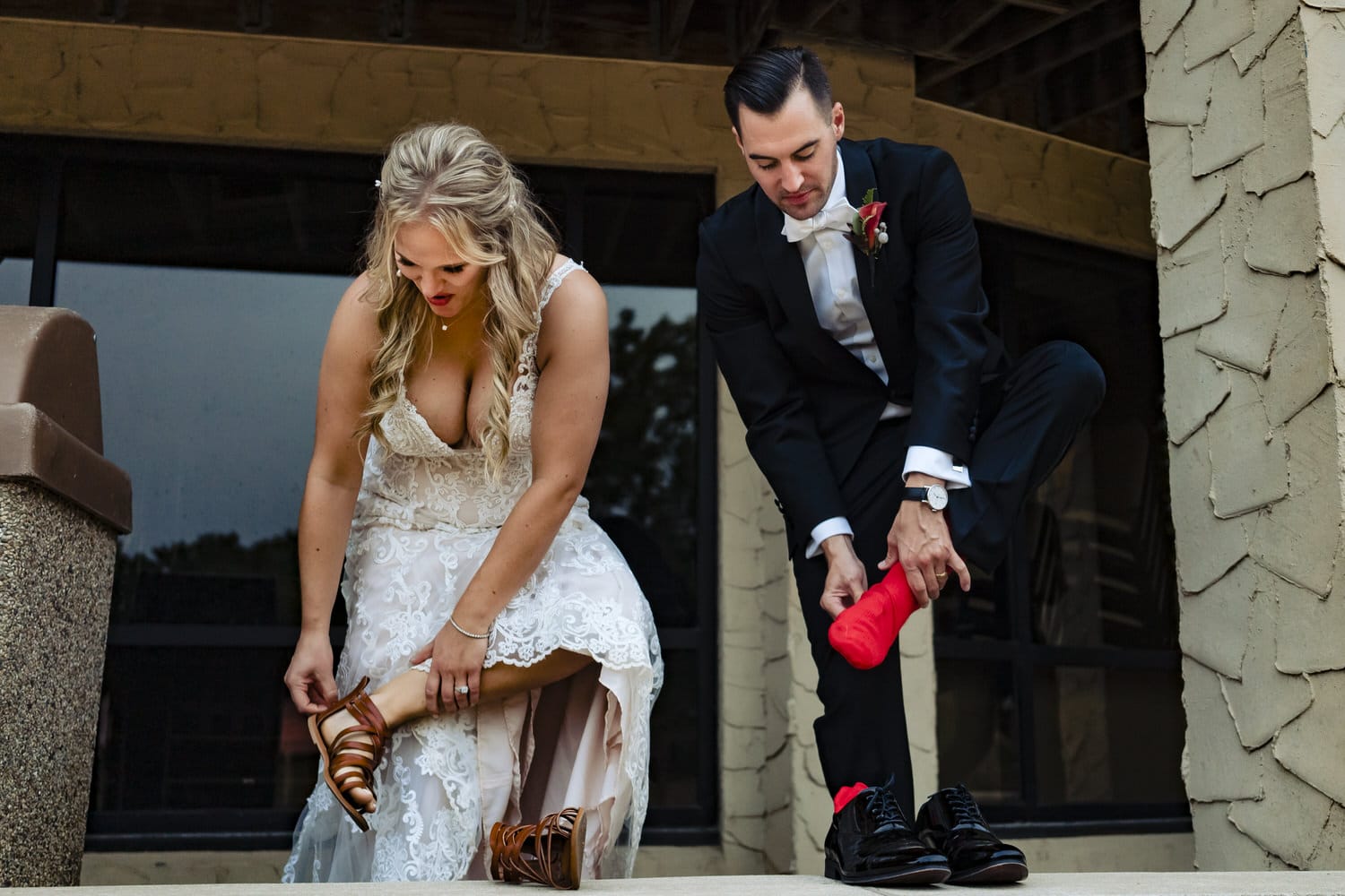 A candid picture of a bride and groom leaning down to put their shoes on. 