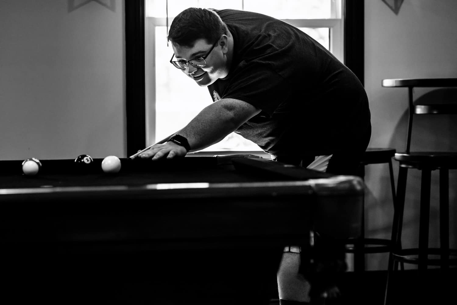 A candid black and white picture of a man playing pool. 