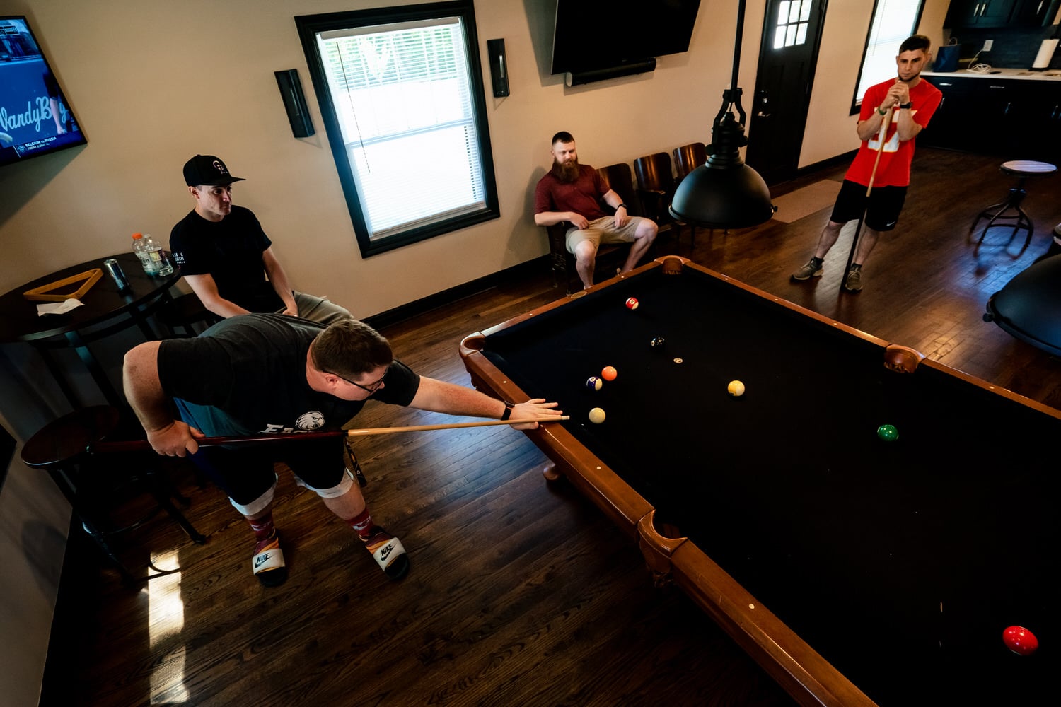 A colorful picture of a group of men playing pool in a small house. 
