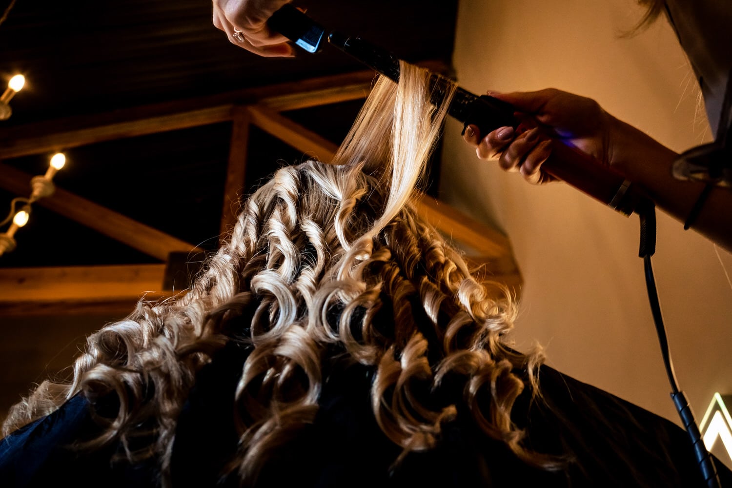 A colorful picture taken from the ground looking up of a hair stylist curling long blond hair. 