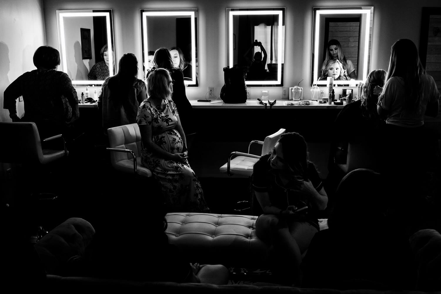 A candid black and white picture of a group of women adjusting their hair and makeup in a row of light-up mirrors on the morning of a summer wedding at The Farmhouse KC Event Venue. 