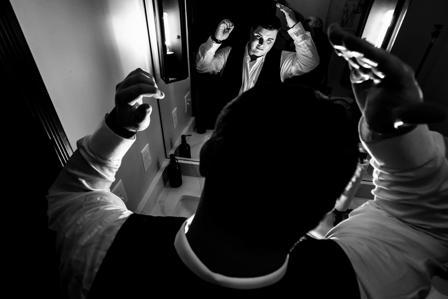A candid black and white picture taken from above of a man messing with his hair in a mirror. 