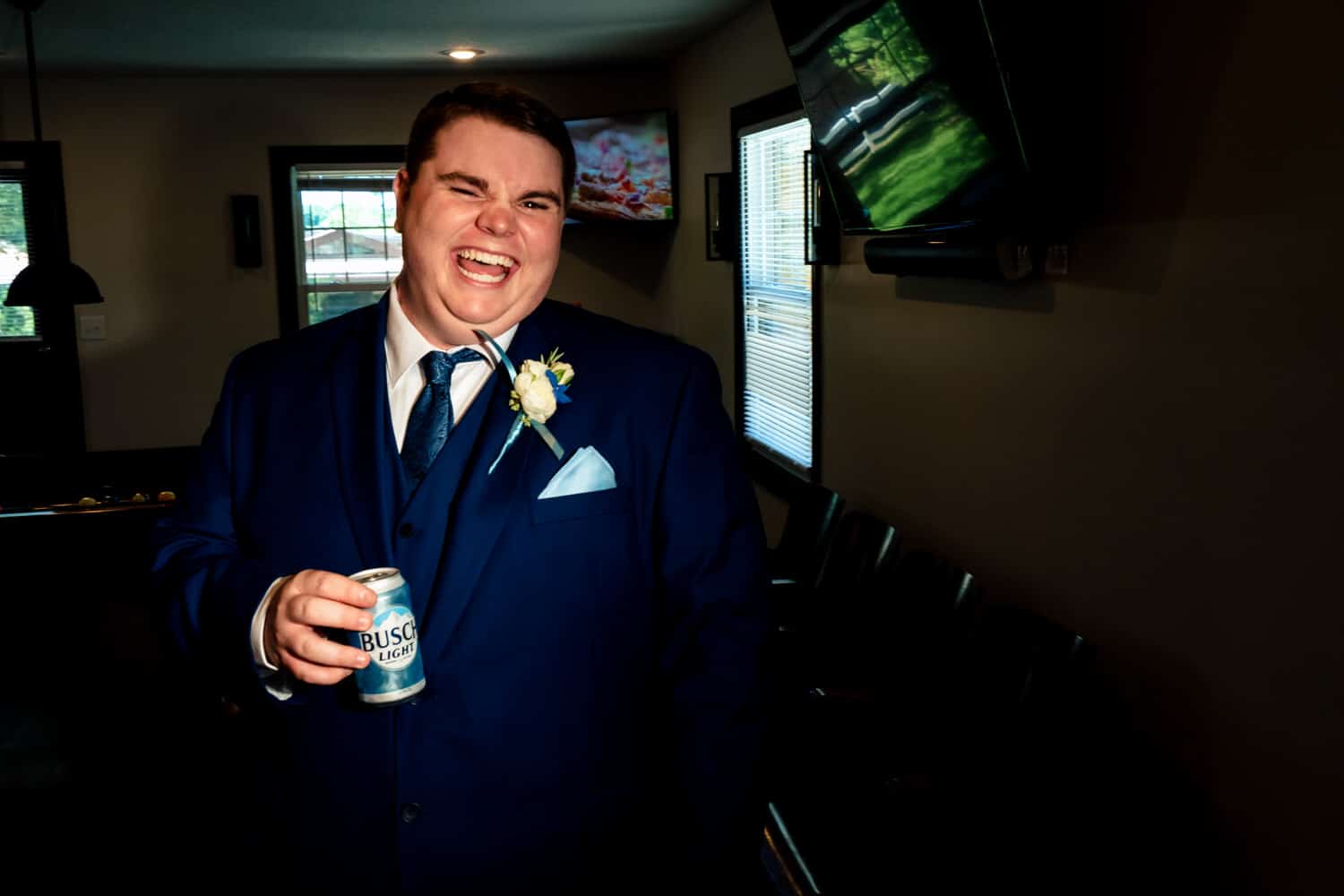 A colorful, candid picture of a groom smiling at the camera, a can of Busch Light in his hand. 
