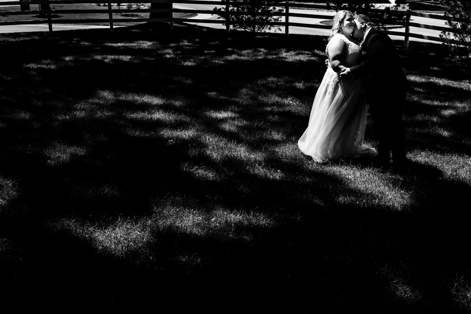 A dramatic black and white picture of a groom leaning in to kiss his bride's neck on their wedding day at The Farmhouse KC Event Venue. 