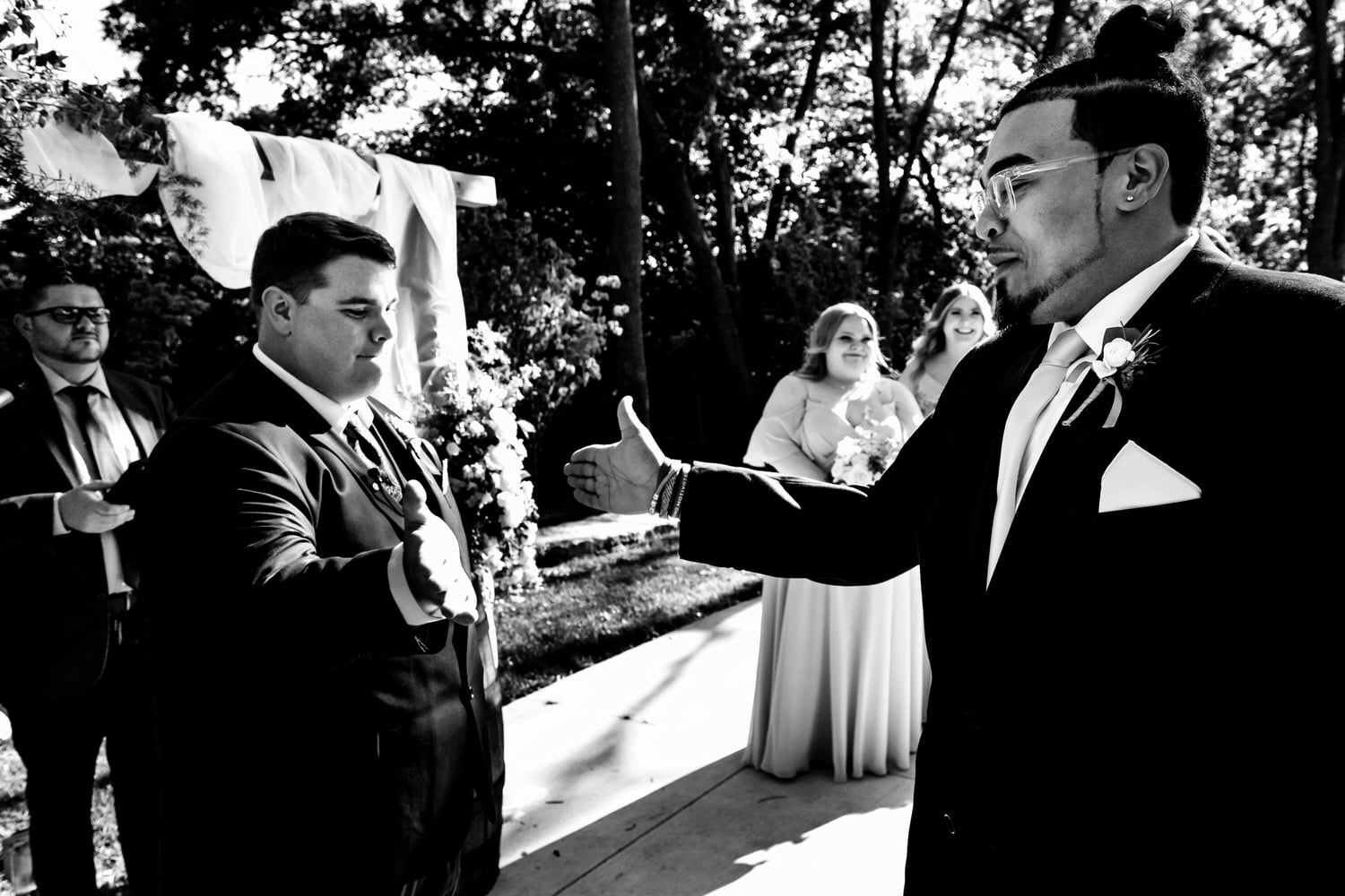 A candid black and white picture of a groom and his best man doing a secret handshake at the beginning of a wedding ceremony at The Farmhouse KC Event Venue. 