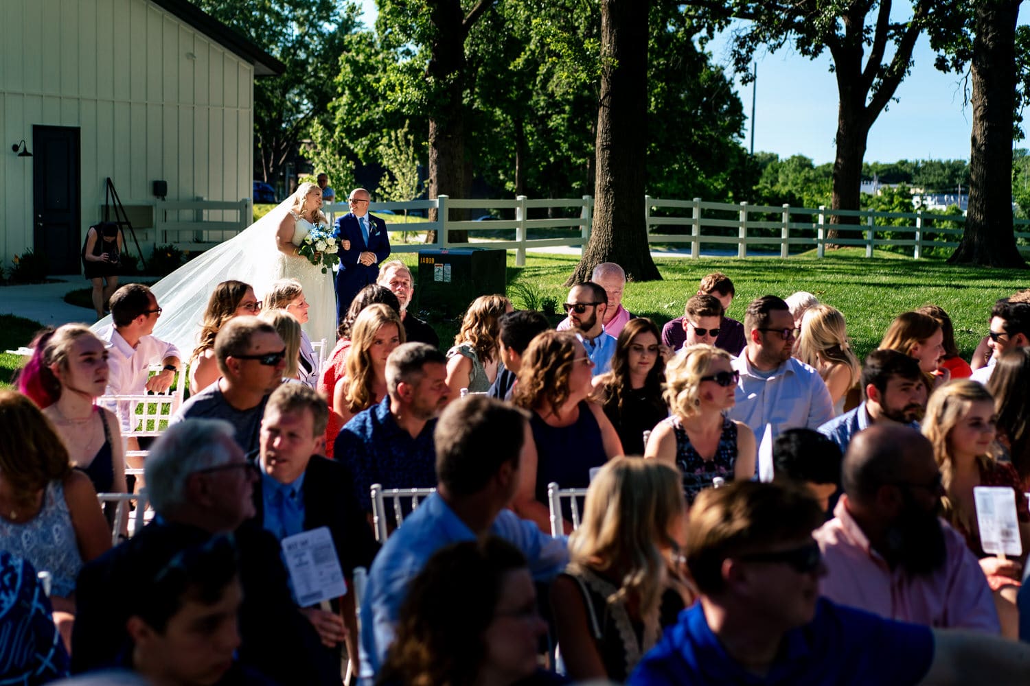 A colorful, candid picture of a bride and her father walking down the aisle on a summer wedding day at The Farmhouse KC Event Venue. 