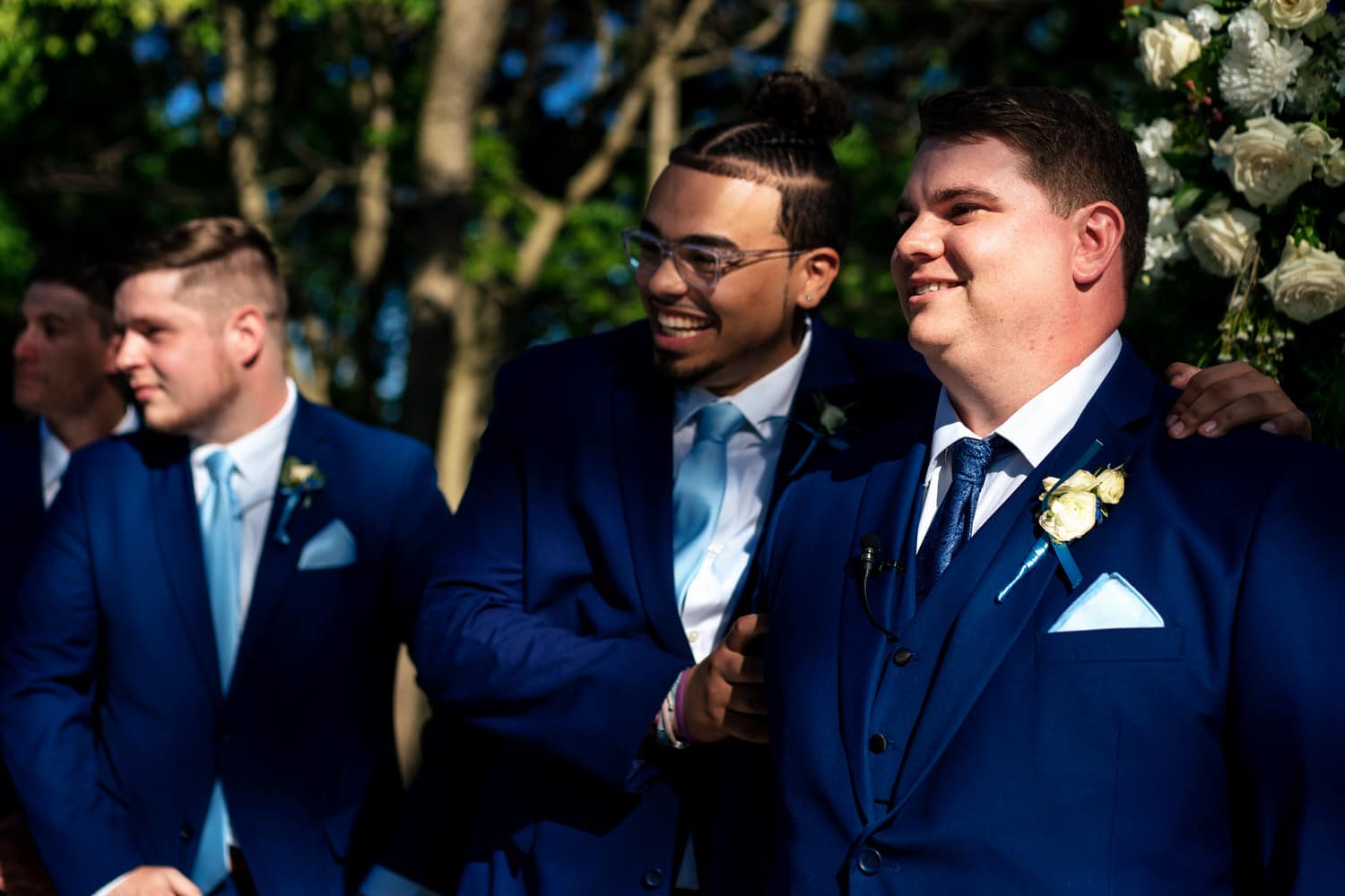 A colorful, candid picture of a best man putting his arm around a groom as he watches his bride walk down the aisle. 