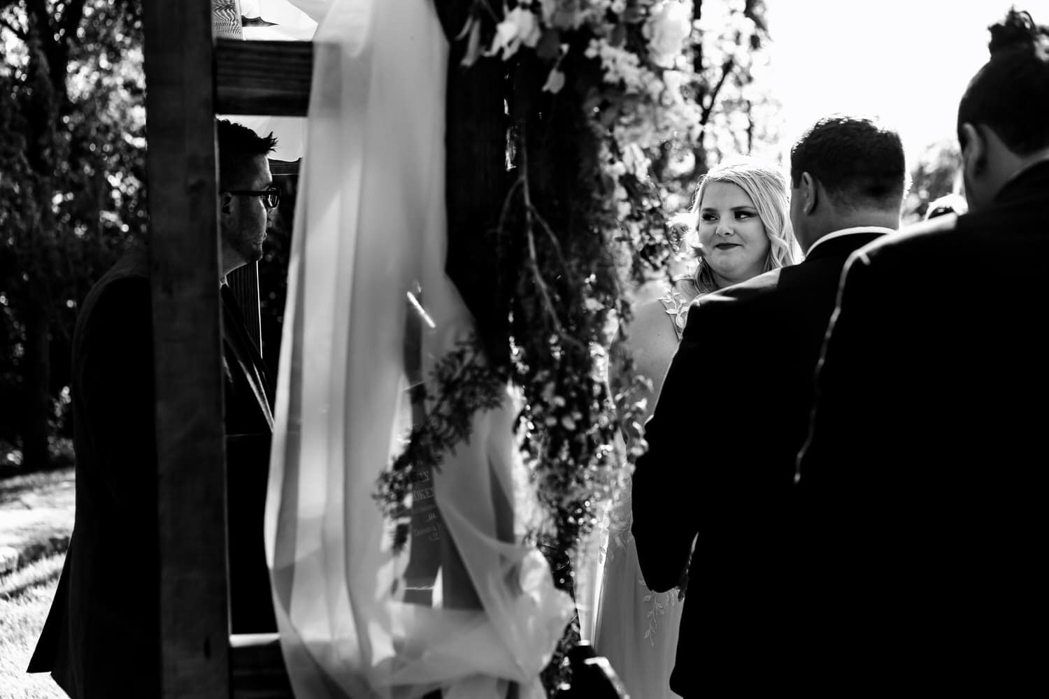 A candid black and white picture of a bride looking at an officiant during a wedding ceremony at The Farmhouse KC Event Venue. 