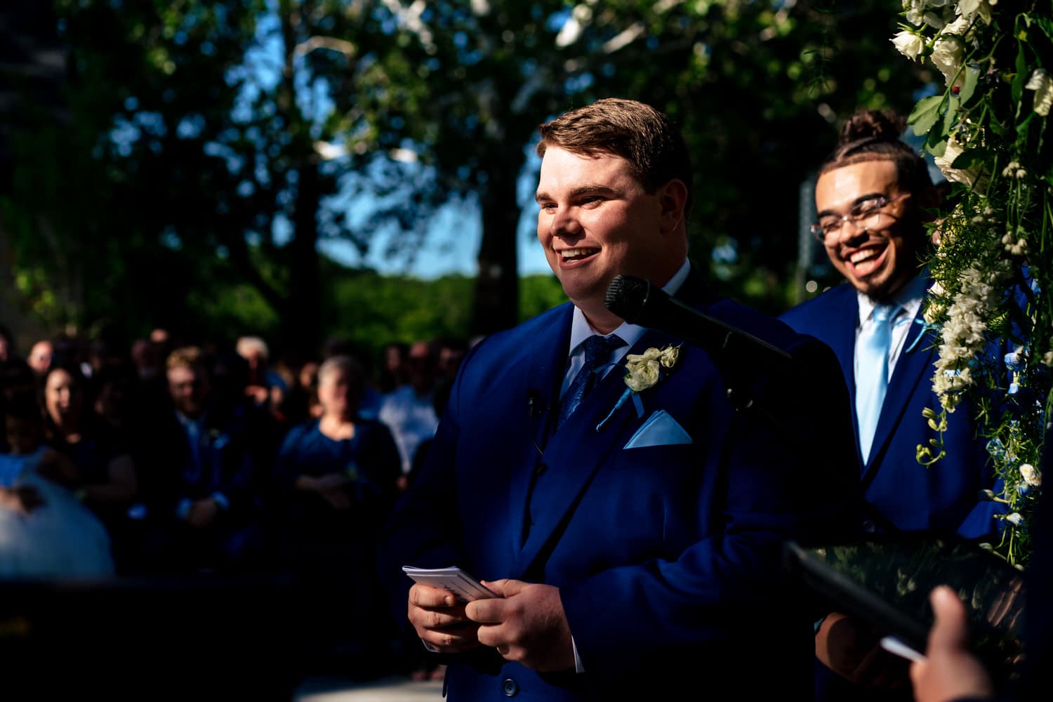 A colorful, candid picture of a groom reading his vows to his bride as his best man laughs behind him. 
