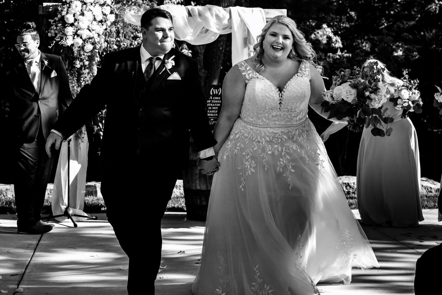 A candid black and white picture of a bride and groom walking up an aisle after their summer wedding ceremony at The Farmhouse KC Event Venue. 