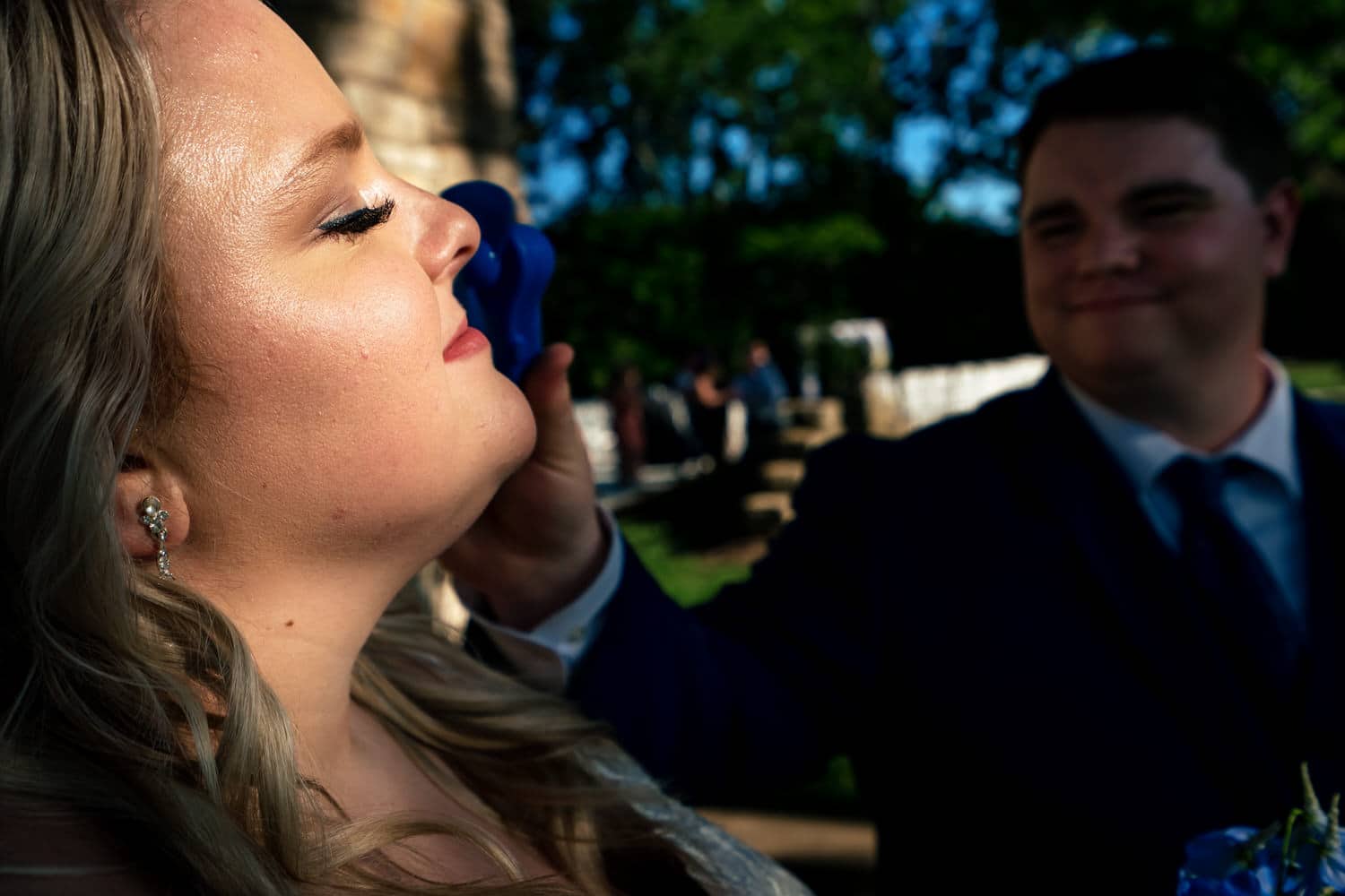 A candid picture of a groom holding a mini, portable fan up to his bride's face on a summer wedding day in Kansas City. 