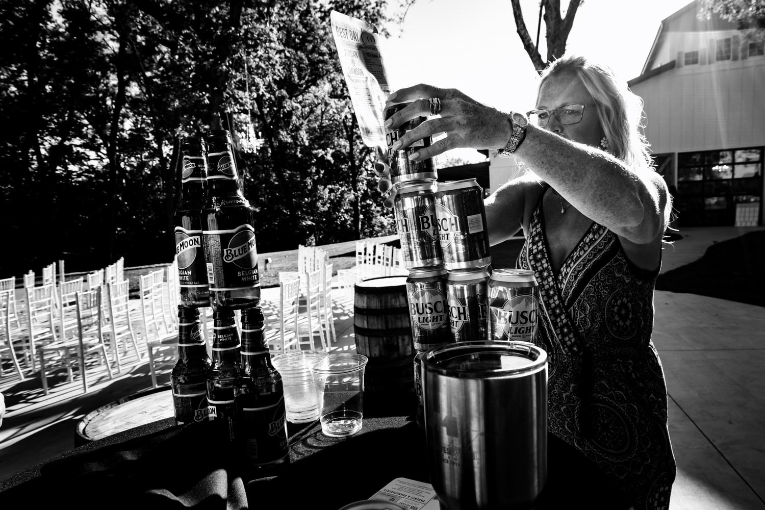 A candid black and white picture of a wedding guest building a tower out of beer cans on a summer wedding day at The Farmhouse KC Event Venue.  