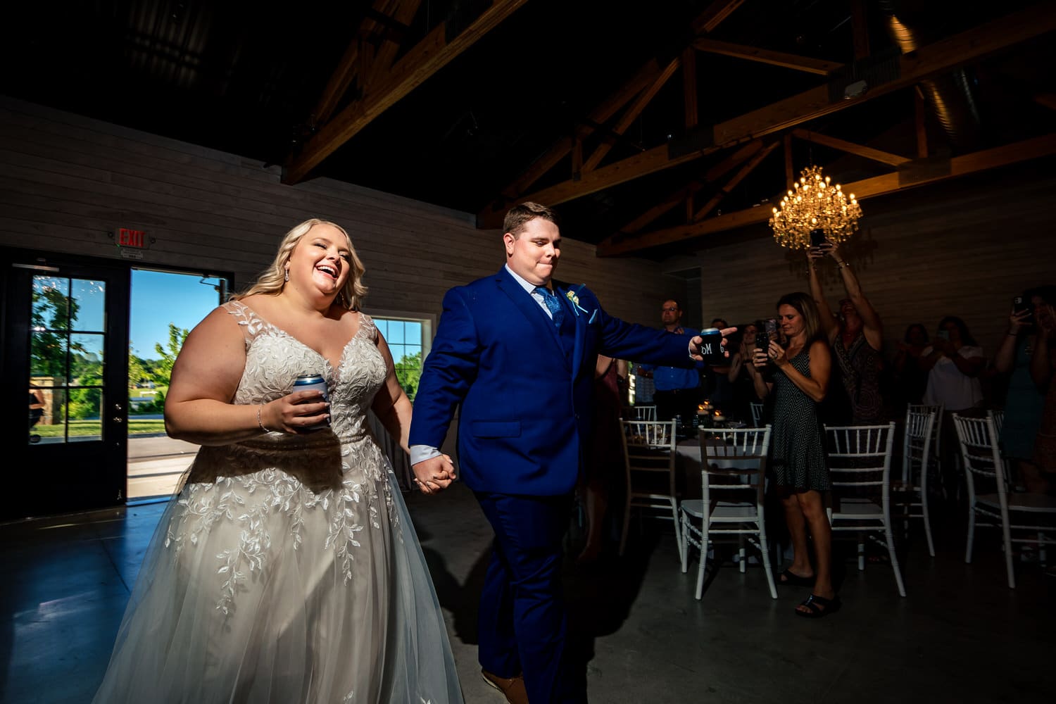 A candid, colorful picture of a bride and groom holding hands and smiling in celebration as they enter their wedding reception at The Farmhouse KC Event Venue. 