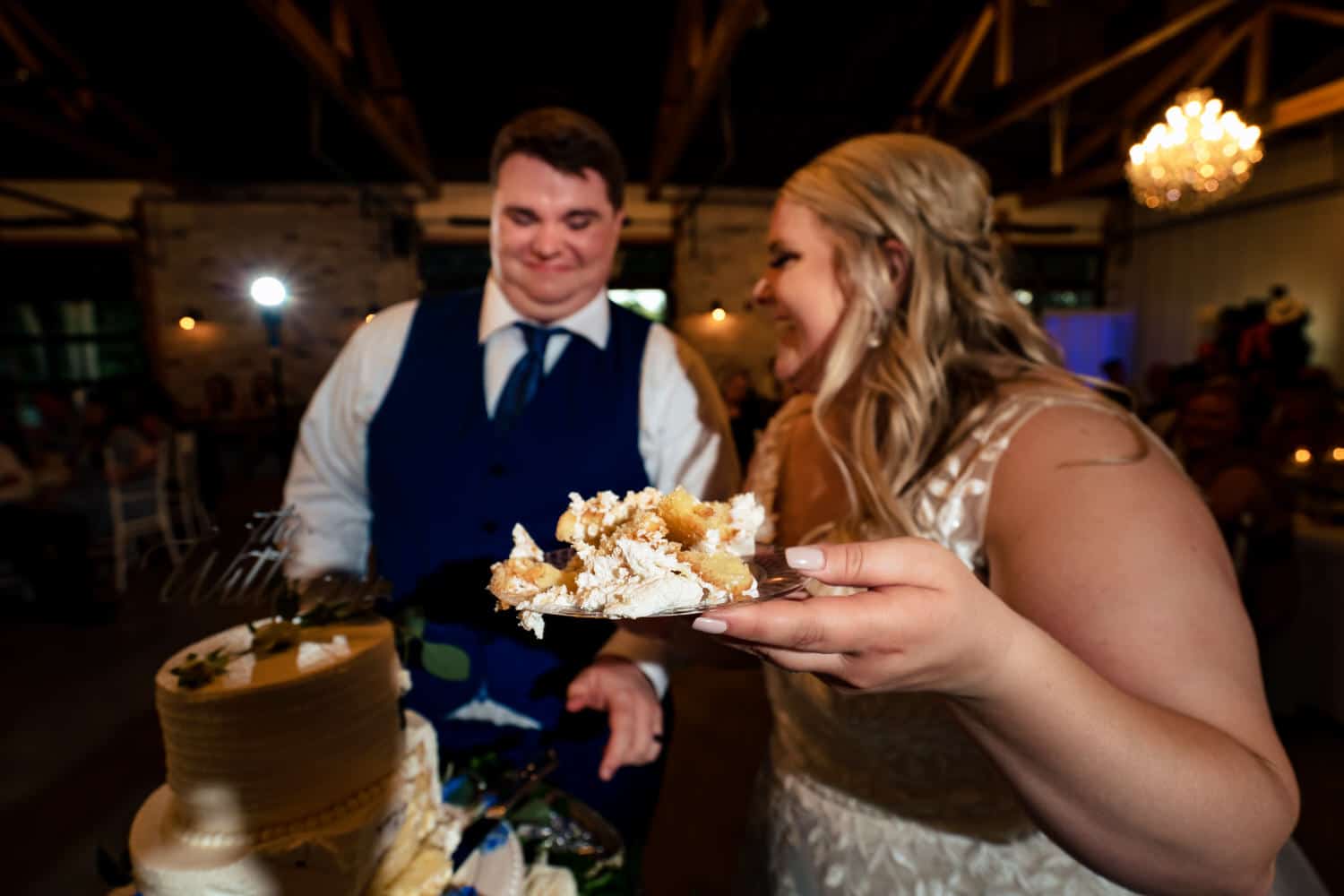 A candid, colorful picture of a bride and groom laughing as they cut a white wedding cake during their summer wedding reception at The Farmhouse KC Event Venue. 