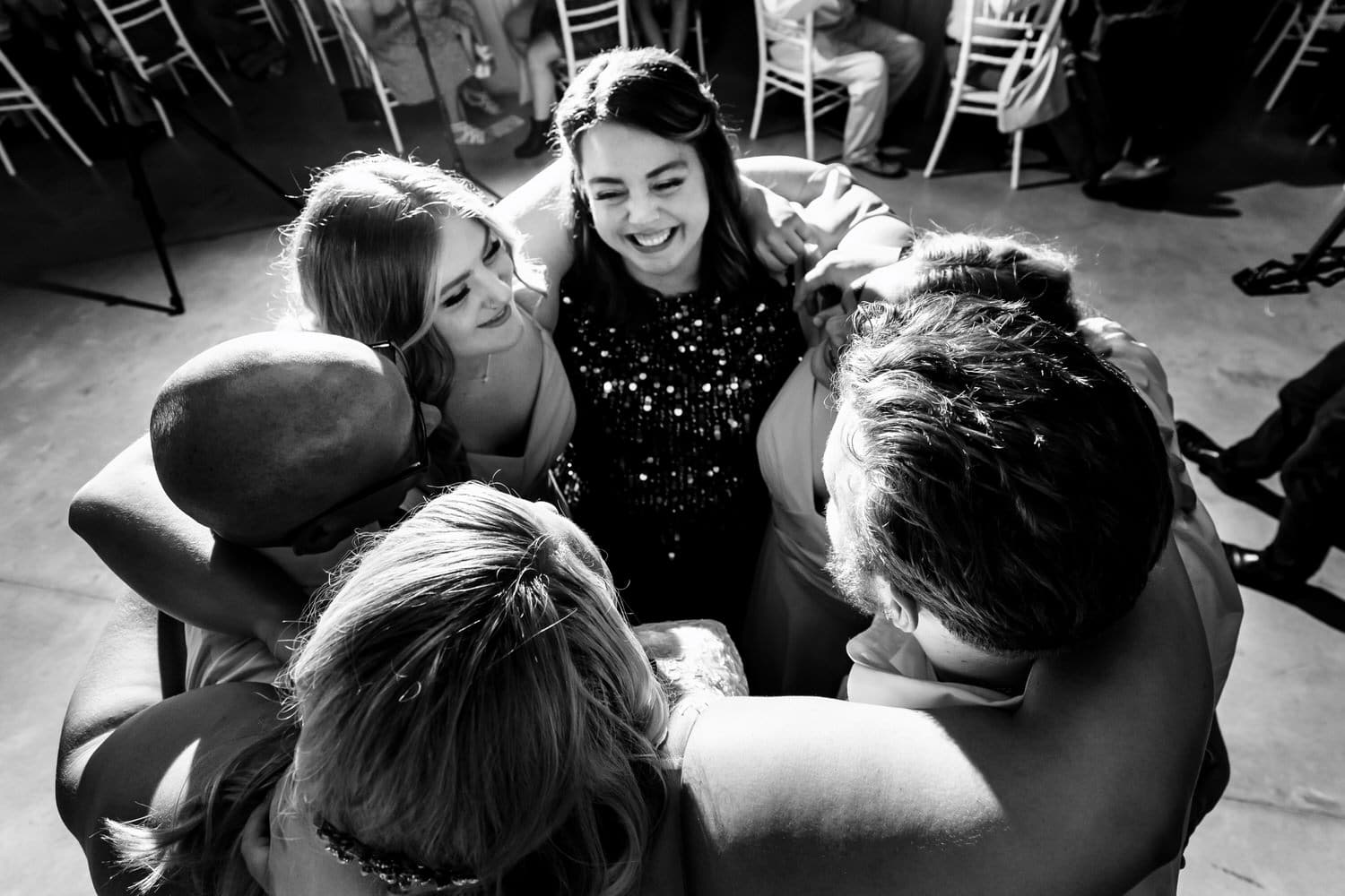 A candid black and white picture of a bride and her siblings dancing in a circle with her parents during a summer wedding reception in Kansas City. 