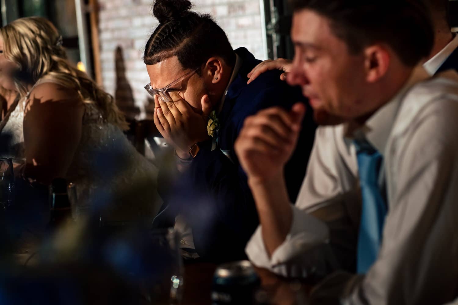 A candid picture of a best man breaking down into tears while a groom dances with his mom during a summer wedding reception. 
