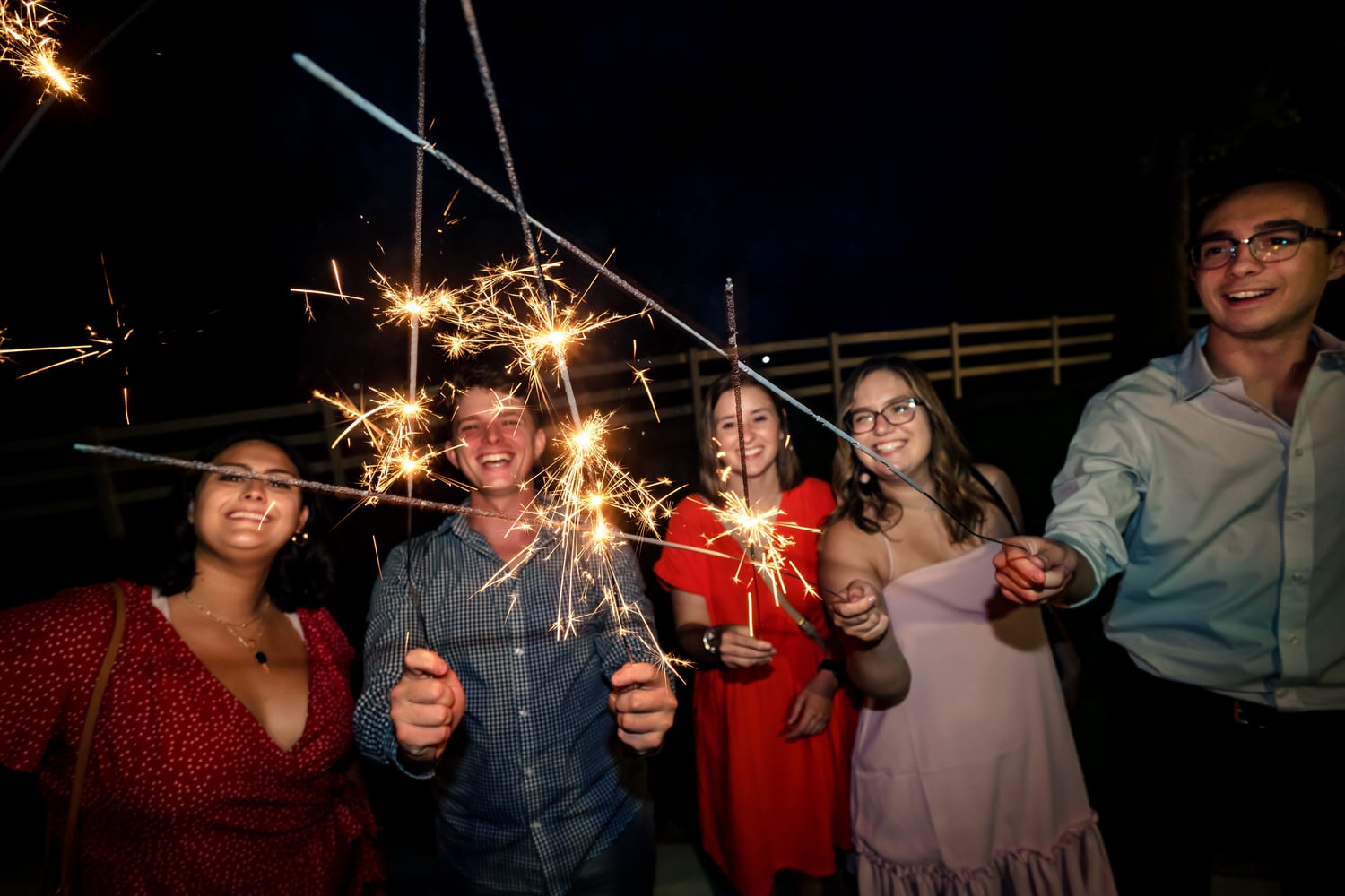 A candid picture of a group of wedding guests holding sparklers up to the camera lens. 