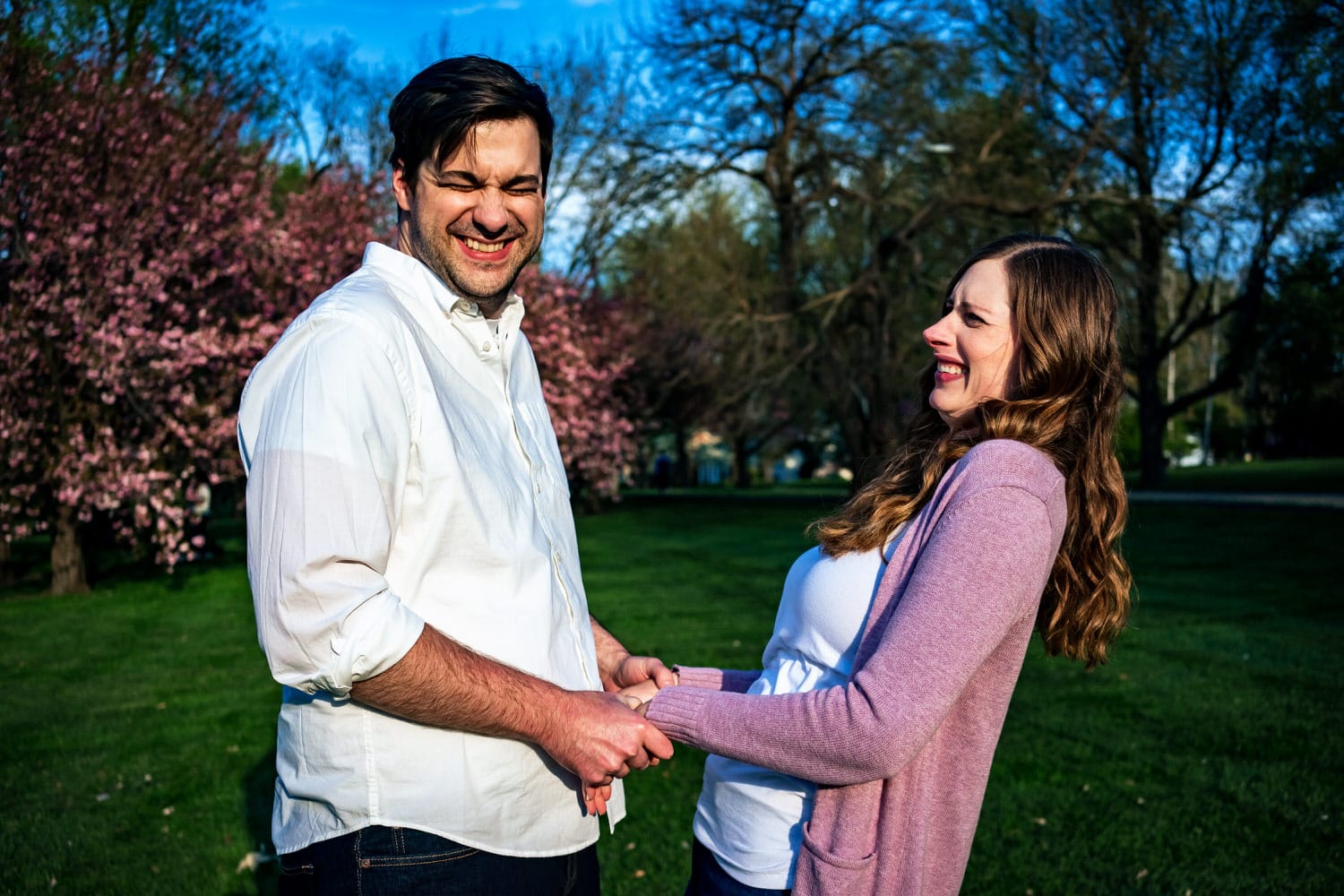 A colorful, candid picture of an engaged couple leaning in to share a kiss in front of a background of cherry blossom trees during their spring engagement session at Loose Park. 
