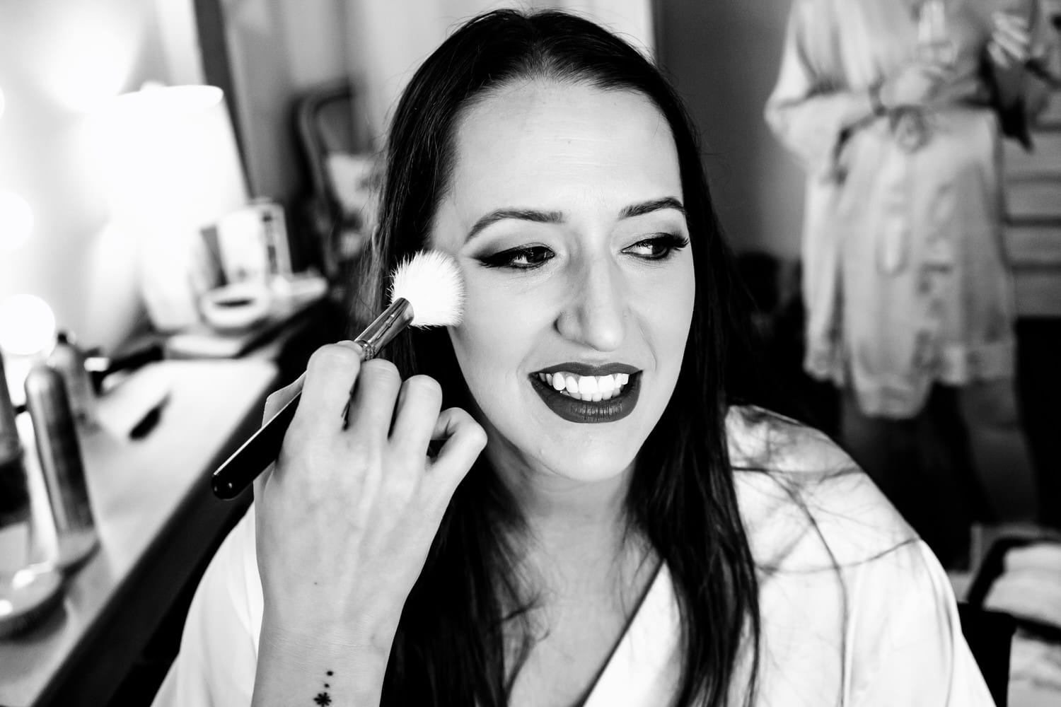 A candid black and white picture of a makeup artist putting powder on a bride's face. 