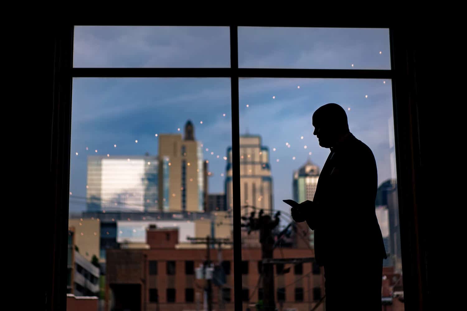A colorful, candid silhouette of a man reading a letter, the Kansas City skyline visible behind him on the day of his summer wedding at The Bauer. 
