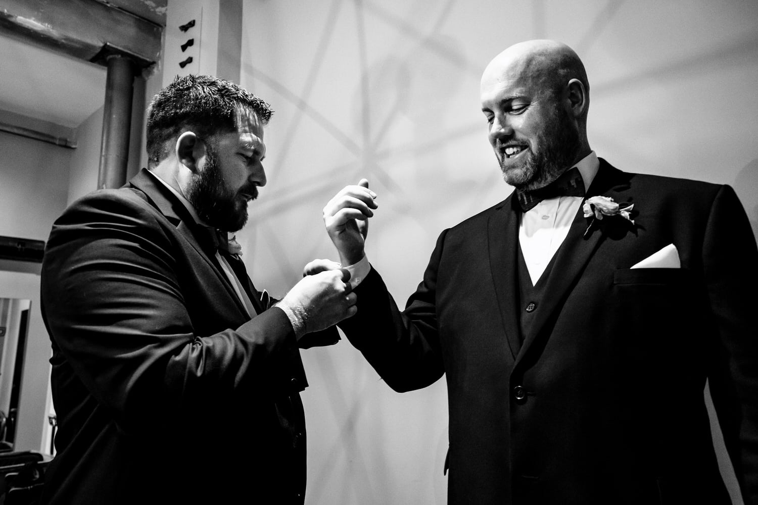 A candid black and white picture of a groomsman adjusting a groom's cufflinks on the day of his wedding. 