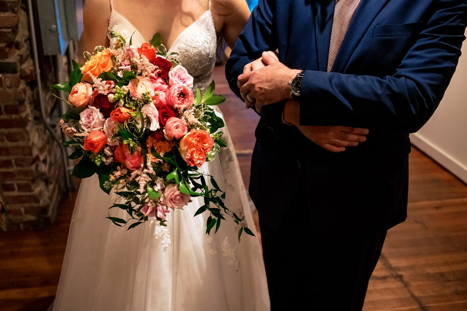 A colorful, candid picture of a bride holding her bouquet, as her dad clutches her hands, moments before walking down the aisle at her summer wedding in Kansas City. 