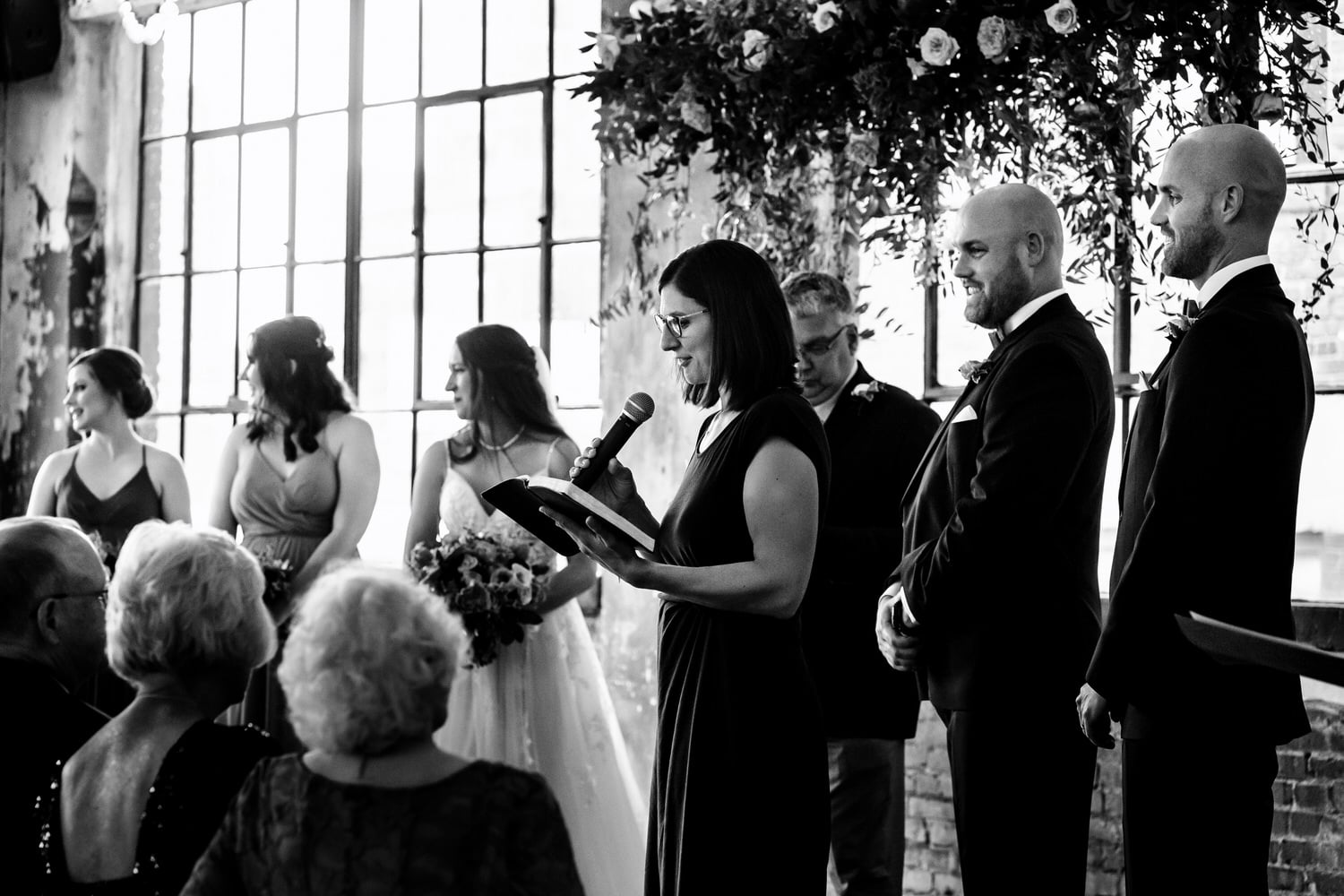 A candid black and white picture of a woman doing a reading during a wedding ceremony at The Bride and The Bauer in Kansas City. 