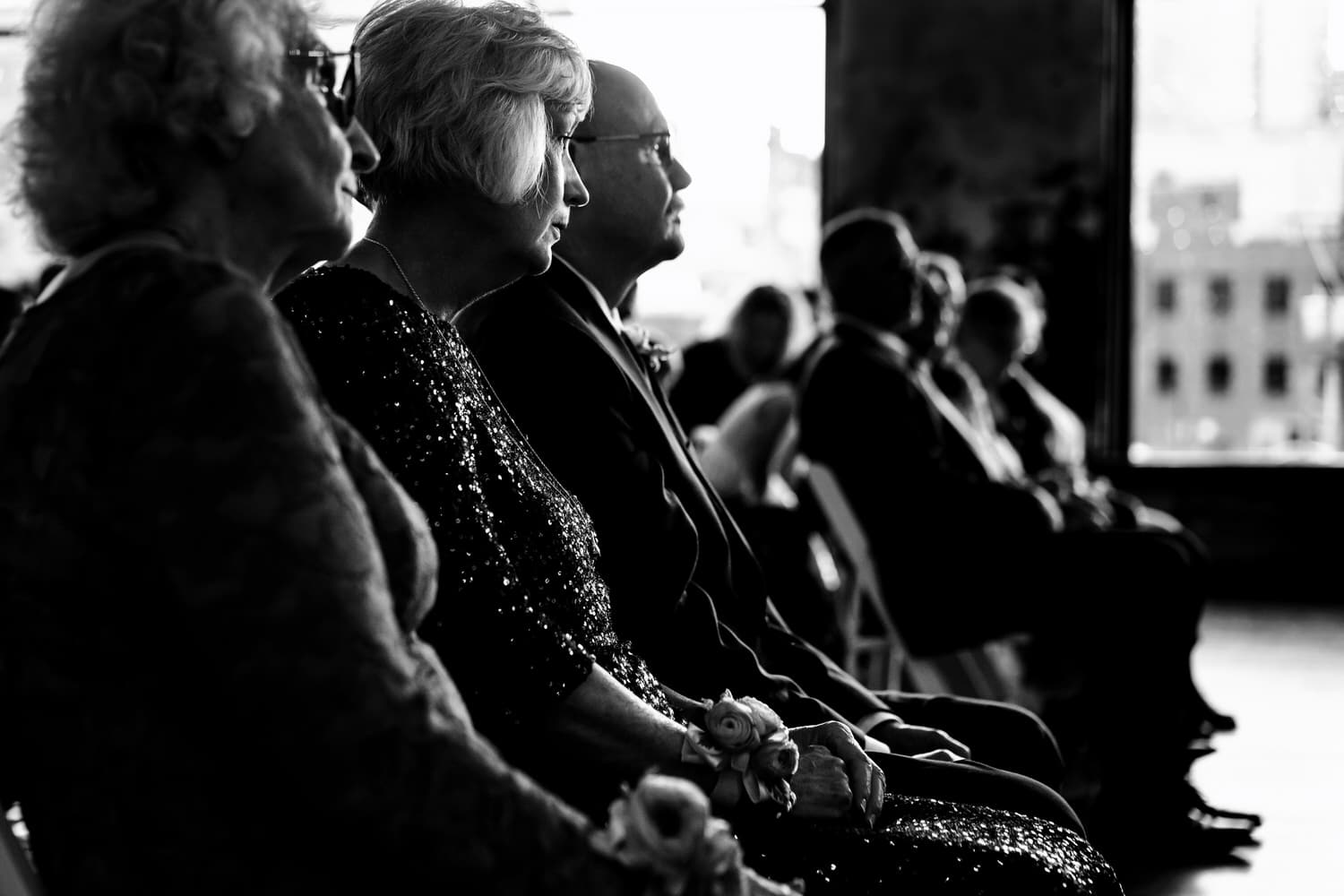 A candid black and white picture, focused on the grooms parents as they watch a wedding ceremony. 