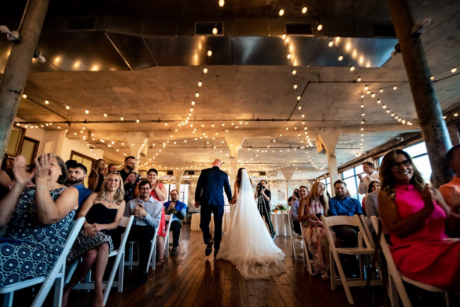 A colorful, candid picture of a bride and groom holding hands, walking back up the aisle after their wedding ceremony at The Bride and The Bauer. 