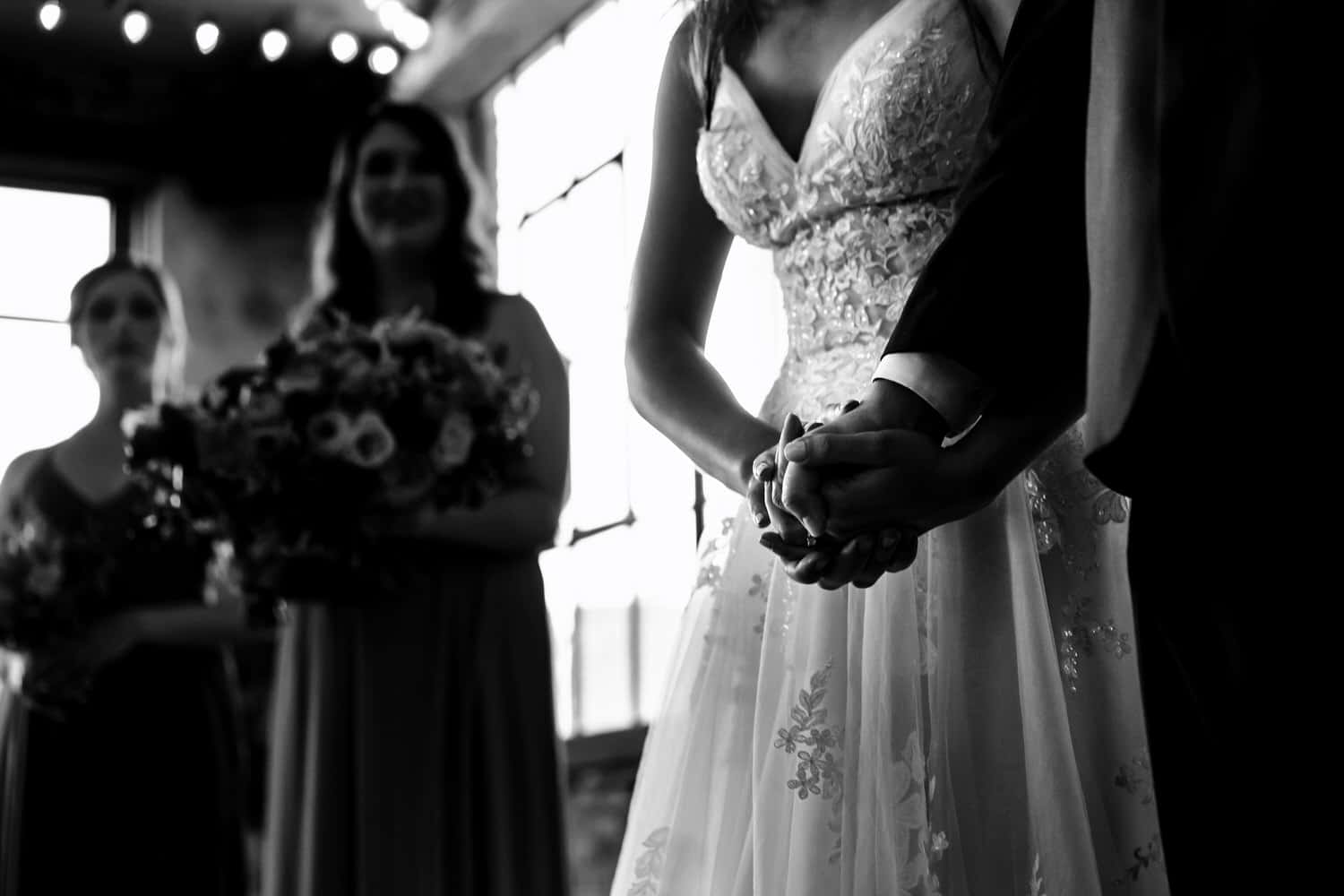 A dramatic black and white picture of a bride clutching her groom's hands at the end of their wedding ceremony at The Bauer in Kansas City. 