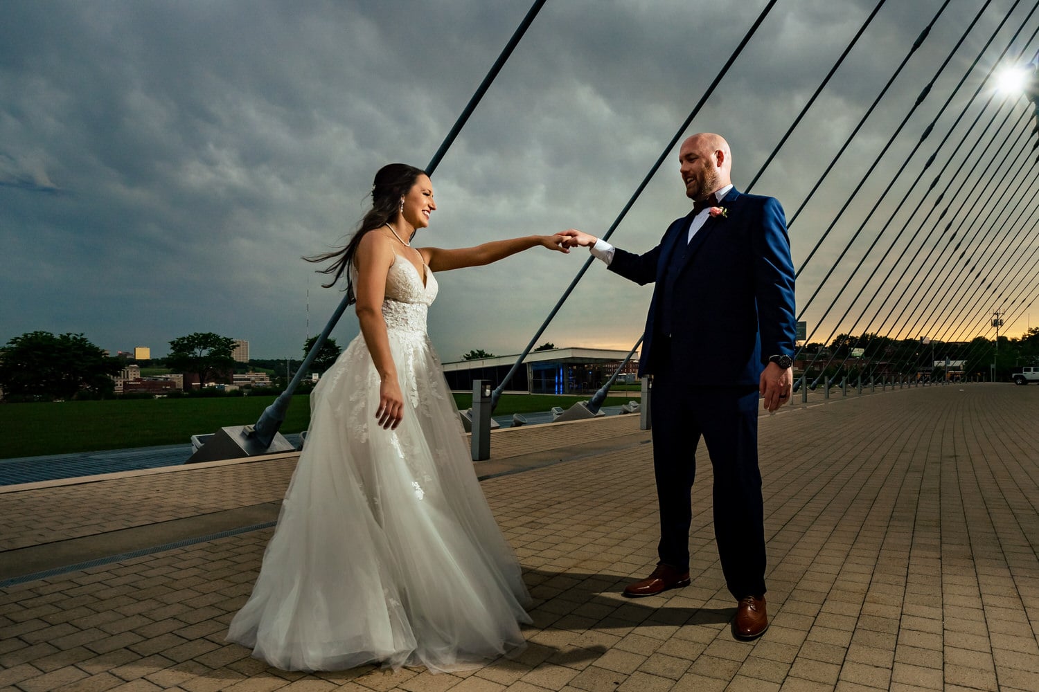 A colorful picture of a bride and groom holding hands, smiling at each other; the Kauffman Center for the Performing Arts visible in the background on their Kansas City wedding day. 