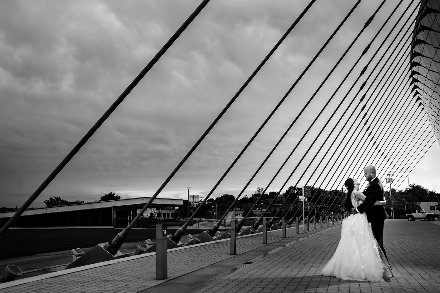 A dramatic black and white picture of a bride and groom holding hands, smiling at each other; the Kauffman Center for the Performing Arts visible in the background on their Kansas City wedding day. 