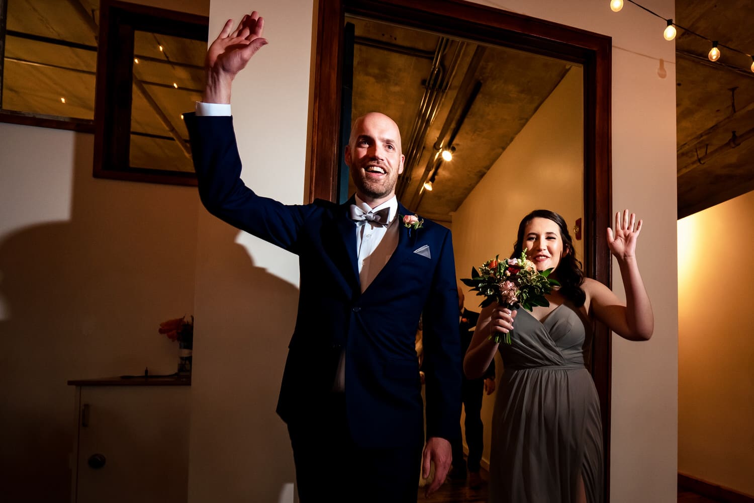 A colorful, candid picture of a bridesmaid and groomsmen waving as they enter a wedding reception at The Bride and The Bauer in Kansas City. 