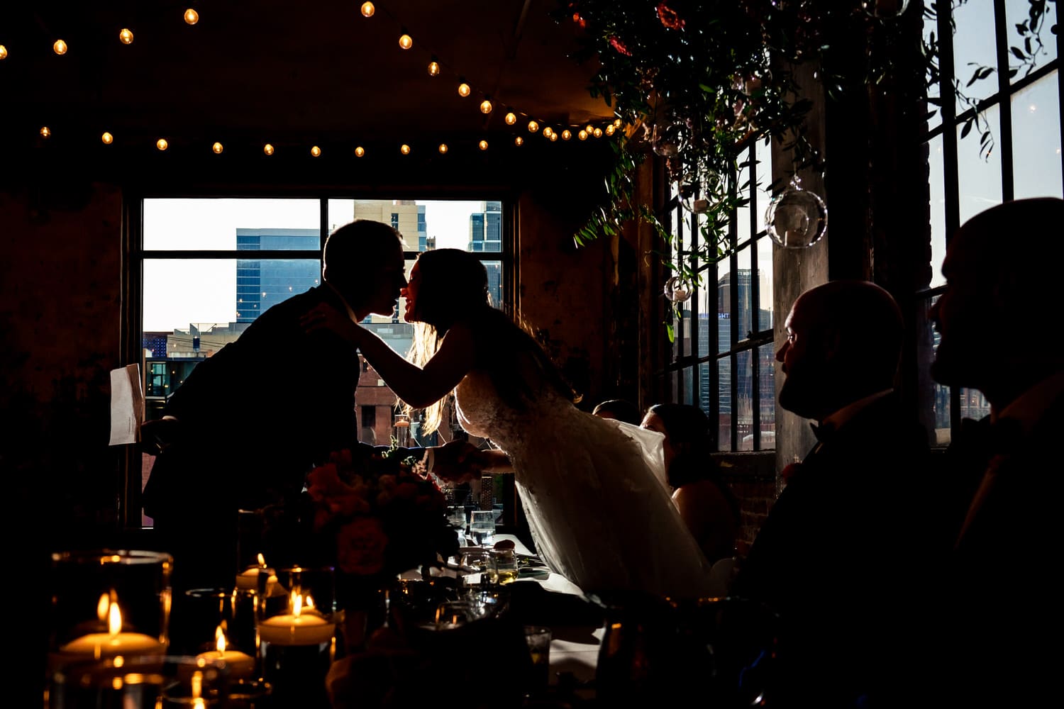 A colorful photo of a bride leaning over the table to kiss her dad on the cheek after his toast at a wedding reception in Kansas city at The Bride and The Bauer. 