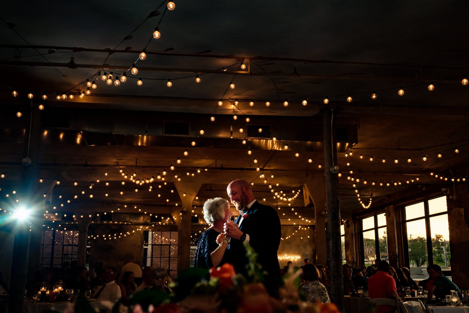 A candid picture of a groom dancing with his mom beneath a canopy of string lights during a summer wedding reception at The Bride and the Bauer in Kansas City. 