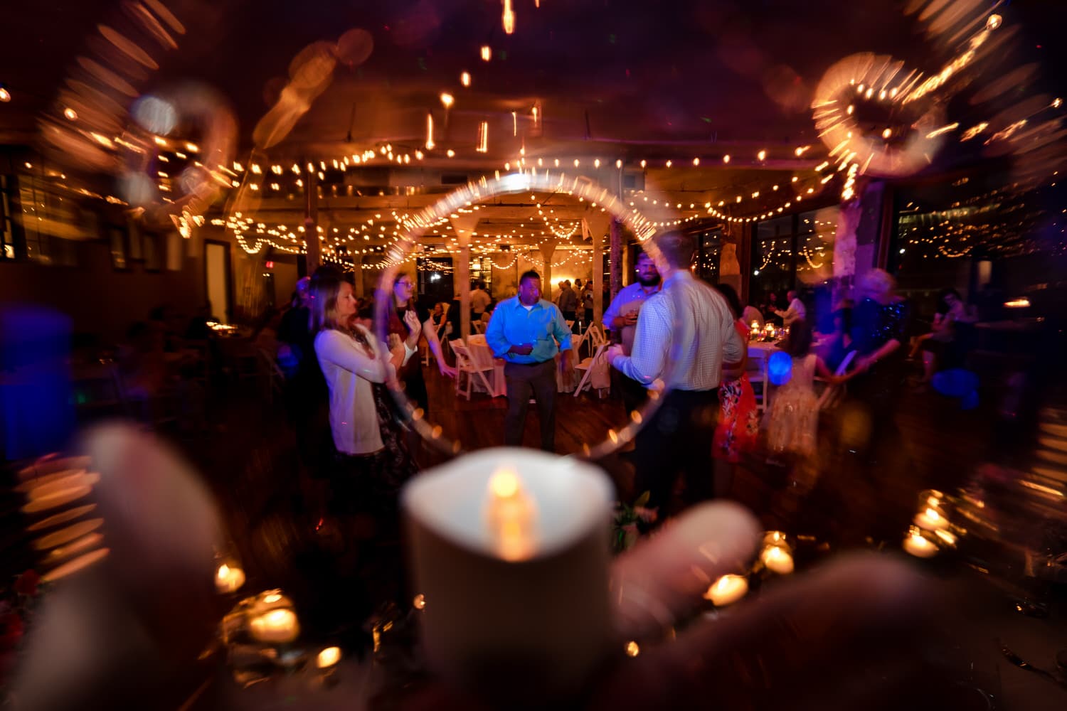 A colorful, wide picture taken through a glass ball of wedding guests on a dance floor during a wedding reception at The Bride and The Bauer in Kansas City. 