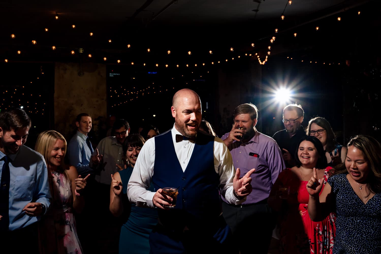 A candid picture of a groom pointing his fingers on the dance floor, surrounding by friends and family members doing the same thing. 