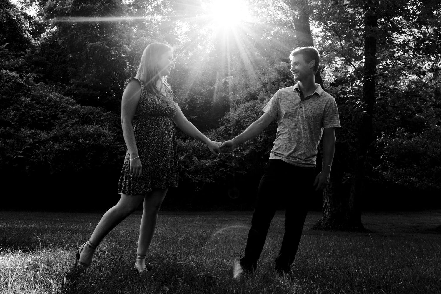 A black and white picture of an engaged couple holding hands and walking across the grass during an engagement session at Wyandotte County Park in Kansas city. 