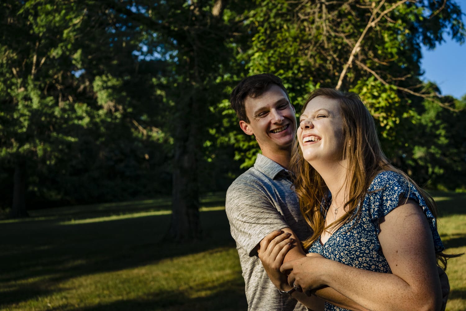 A colorful, candid picture of an engaged couple laughing together as they share an embrace during their summer engagement session at Wyandotte County Lake in Kansas City. 