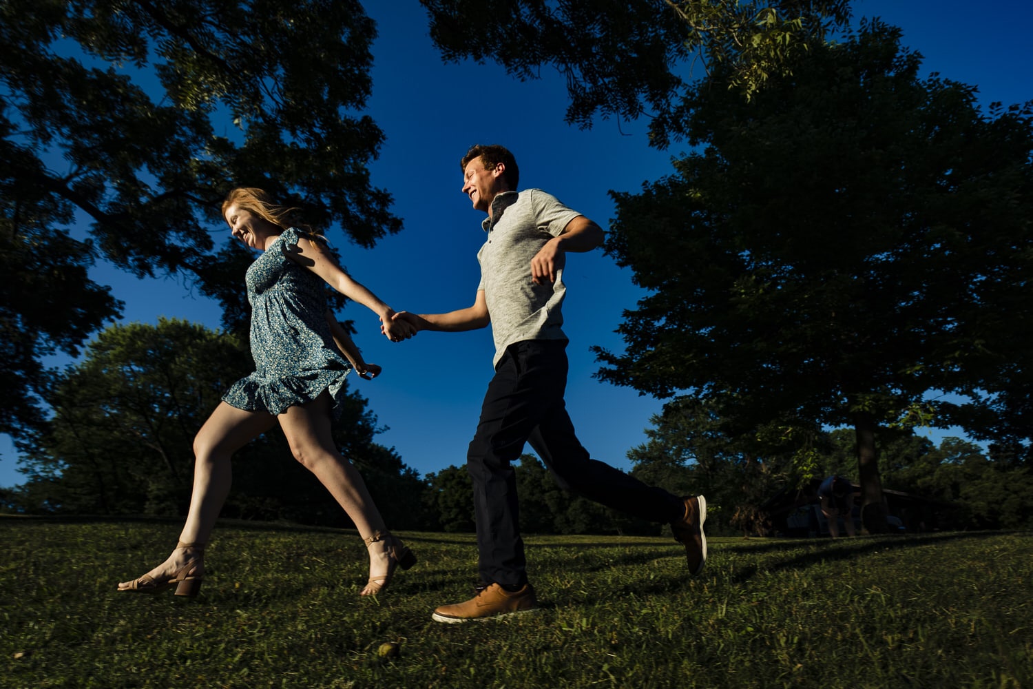 A colorful picture of an engaged couple holding hands running across the grass during an engagement session at Wyandotte County Park in Kansas City. 