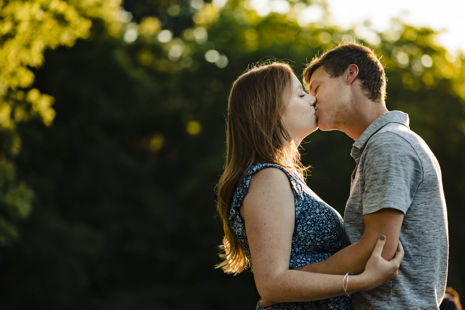 A colorful portrait of an engaged couple sharing an embrace and kiss during their summer engagement session at Wyandotte County Park in Kansas City. 