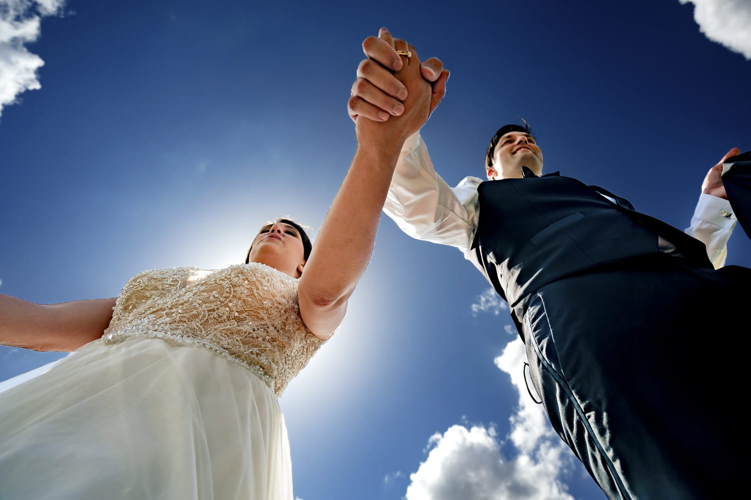 A candid picture taken from the ground looking up of a bride and groom, holding hands, walking over the camera on a summer wedding day in Kansas City. 